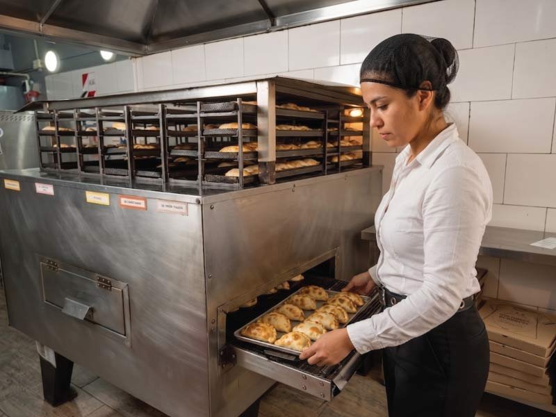 Cocinera retirando una bandeja de empanadas recién horneadas
